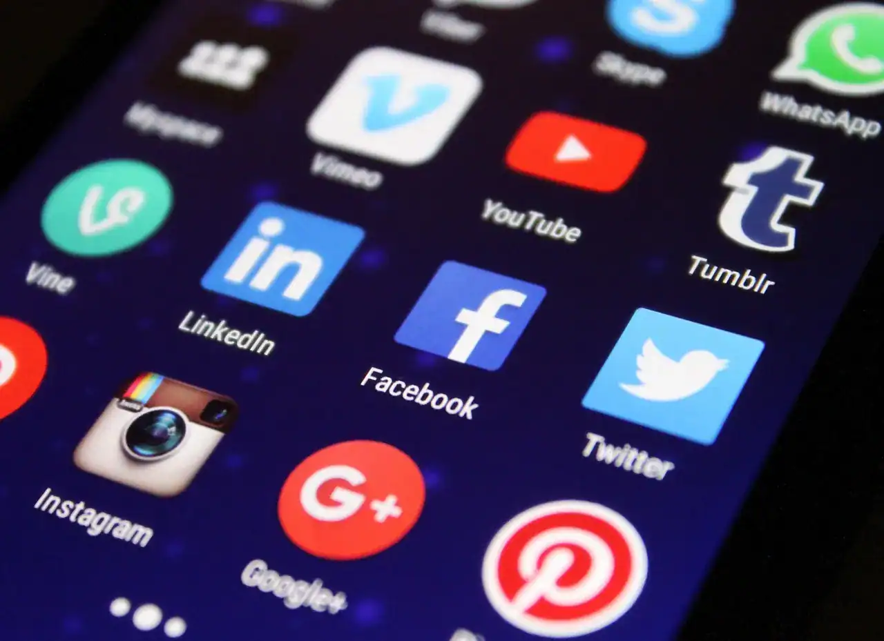 Close-up of a smartphone screen displaying various social media app icons including Facebook, Twitter, Instagram, and LinkedIn.
